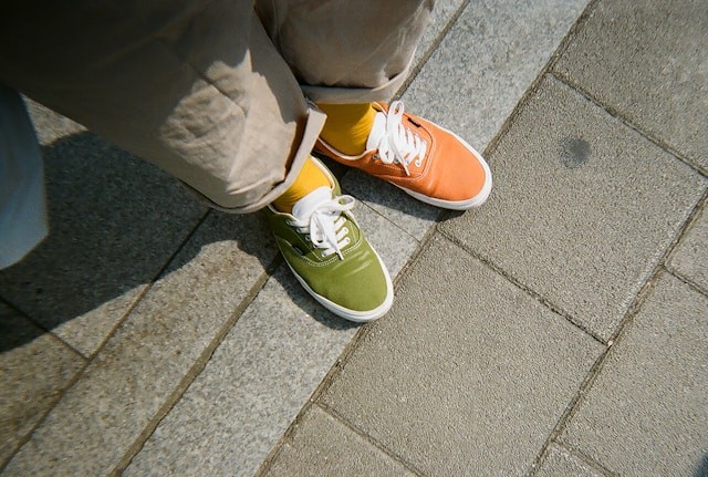 A person with two shoes, one is green, one is orange